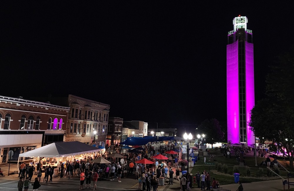 Large photo of Downtown Jefferson, Iowa at night. The Mahanay Bell Tower is glowing with purple light.