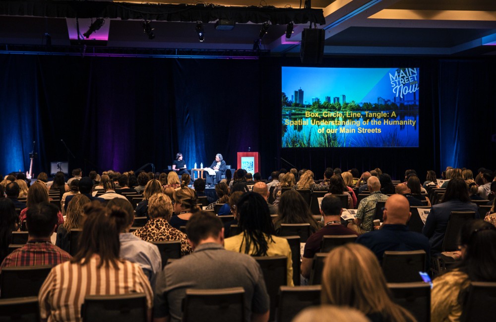 An audience listens to a conversation between two people seated on a stage.