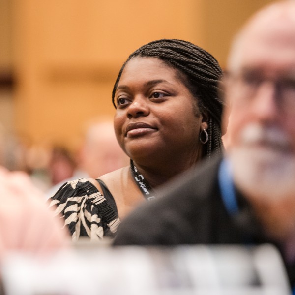 People listen intently to a speaker; in the center and in focus is a woman smiling.