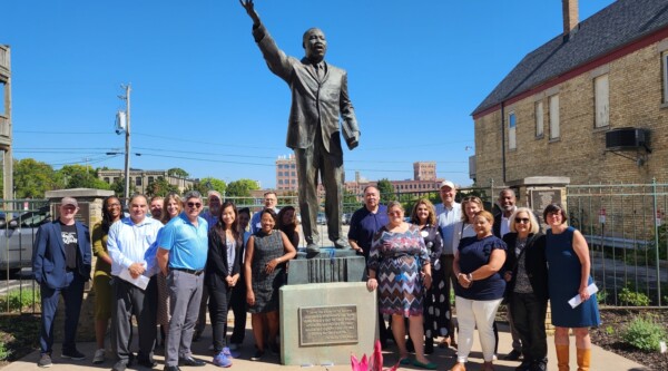 A large group of people poses next to a statue of Martin Luther King Jr. under a clear blue sky