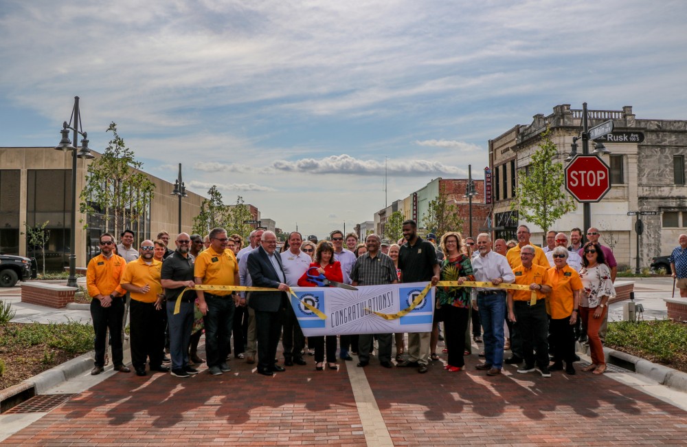 Dignitaries celebrating with banner on paved road. Banner reads "Congratulations!"
