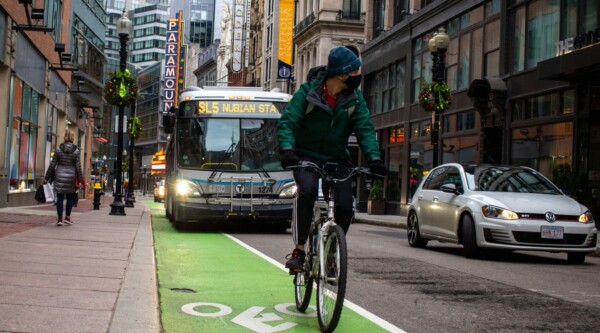 In Boston, a man bikes in a bike lane will a bus drives in the lane next to him.
