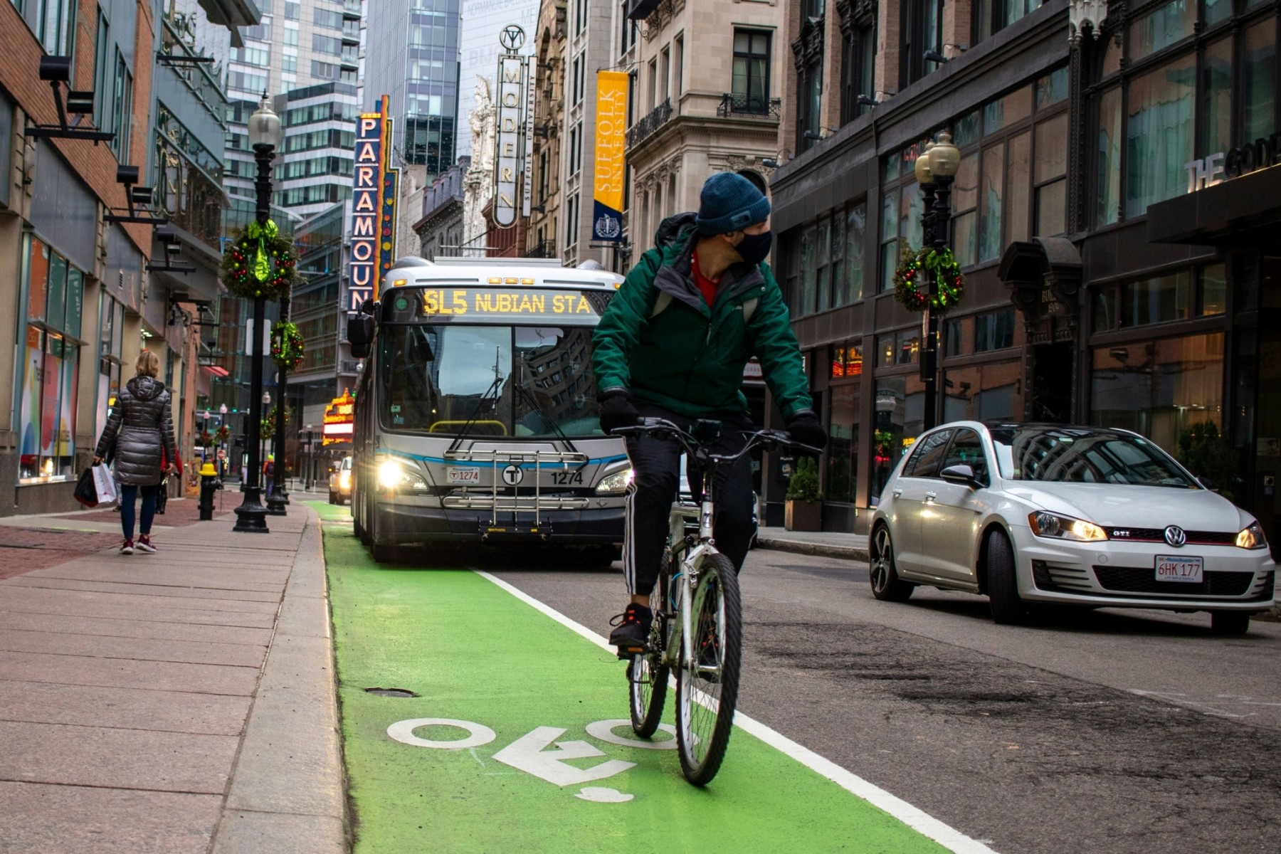 In Boston, a man bikes in a bike lane will a bus drives in the lane next to him.