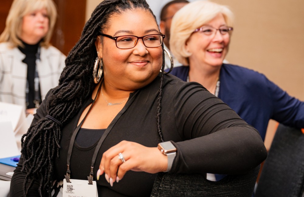 Two women smile while listening to speakers.
