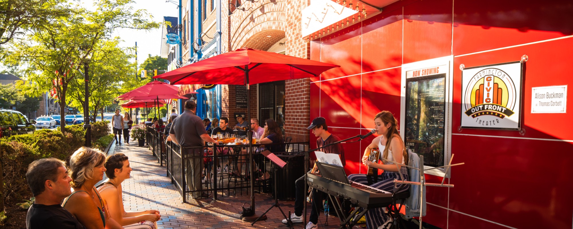 A group of people listening to buskers playing music outside a small business on a sunny street