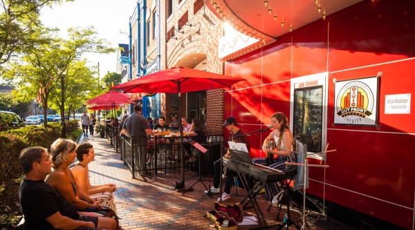 A group of people listening to buskers playing music outside a small business on a sunny street