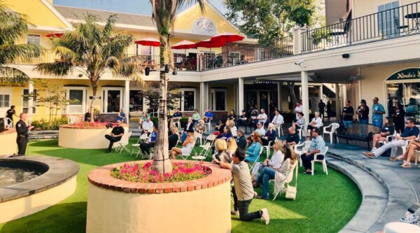 A large group of people seating on an outdoor grassy patio during a community meeting