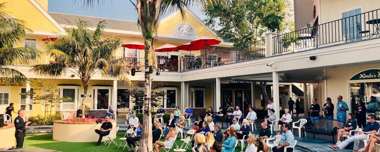 A large group of people sitting on a grassy lawn during a community meeting