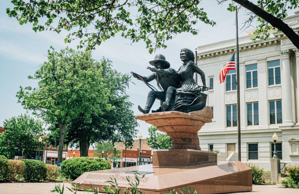 Statue framed by tree branches with the Noble County Courthouse in the background.