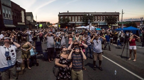 A crowd gathers in downtown Sweetwater, Tennessee to view the 2017 Total Solar Eclipse. All wear protective eyewear and gaze up toward the sky.