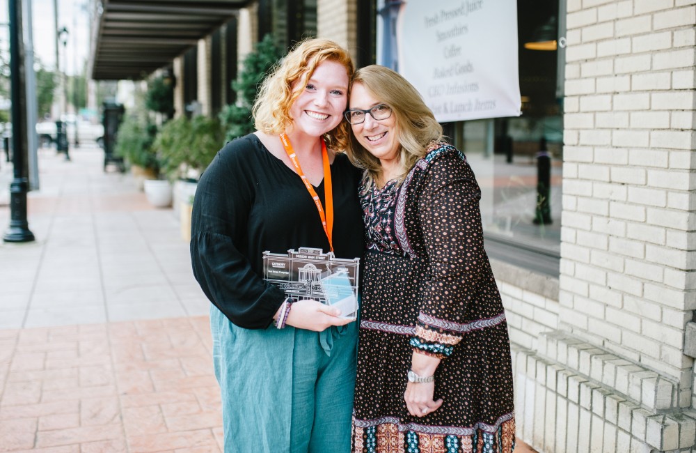 Two woman posing with Excellence on Main Award