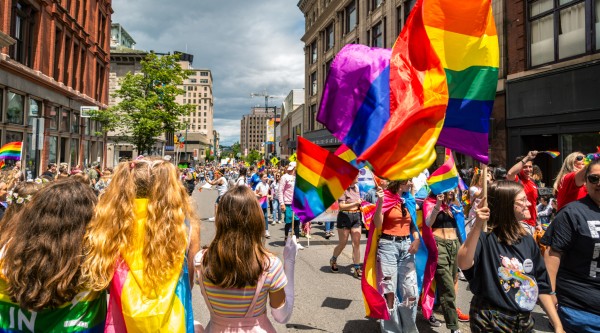 A group of people in colorful clothing carrying rainbow flags march in a Pride parade