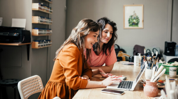 Two woman sitting at a desk looking at a laptop