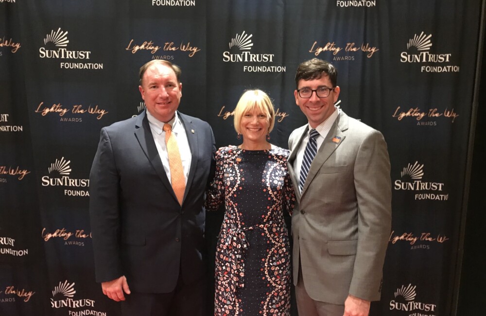 Two men and woman pose in front of a larger SunTrust banner.