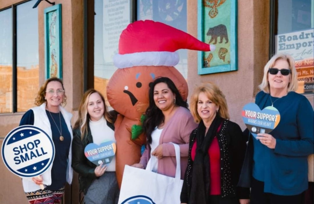 Group of women posing in front of a storefront holding signs that read "Shop Small."