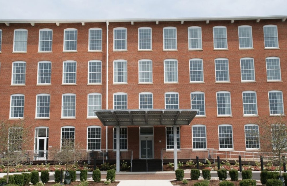 Exterior of a restored brick mill with new windows and shrubbery.