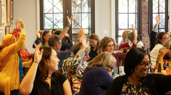 A diverse group of people raise their hands while participating in a seminar.