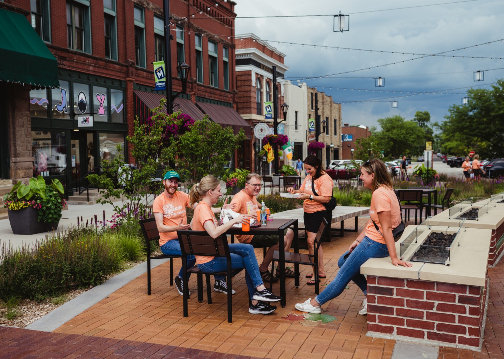 A group of people in matching t-shirts sitting around a table in an outdoor patio area on a Main Street