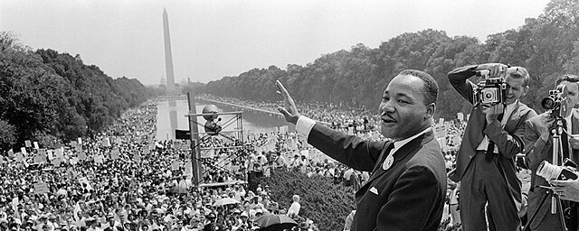 Black and white photo of Martin Luther King Jr. delivering a speech to a large crowd in DC