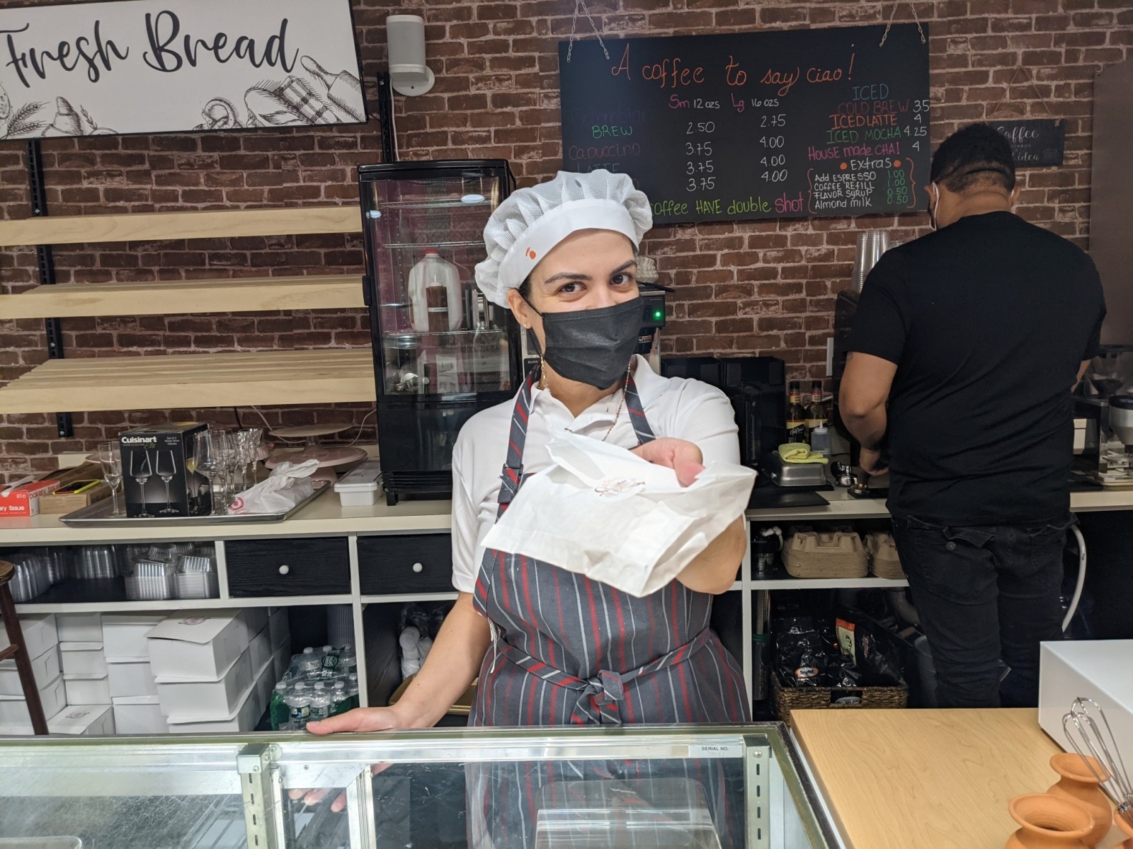 A woman in a chef hat and apron hands a pastry over a counter