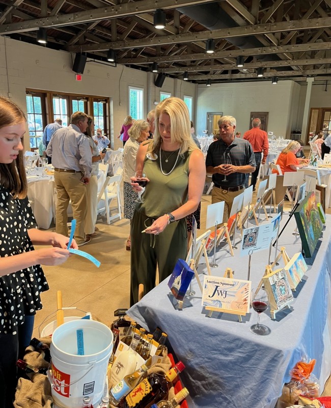 Inside a large room filled with artworks on display, a volunteer hands tickets to a woman.