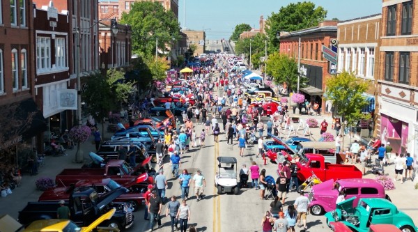A busy street fair with vintage cars in a historic downtown on a sunny day