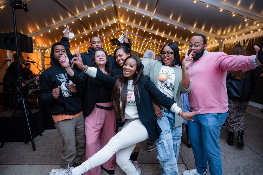 A small group of people smile and raise their arms in celebration while attending a party inside an illuminated tent.