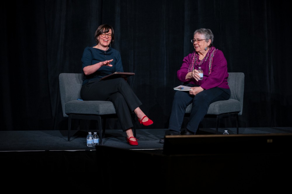 Two women smile as they host a fireside chat-style conversation.