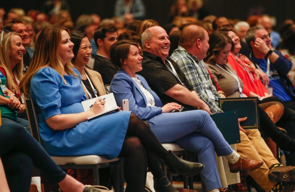 People sitting theater-style in a large room, laughing along with a speaker (not pictured).