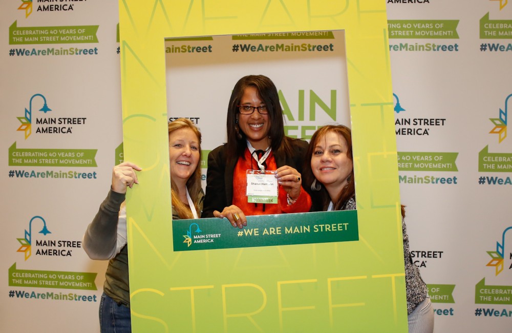Three people pose with an oversized picture frame.