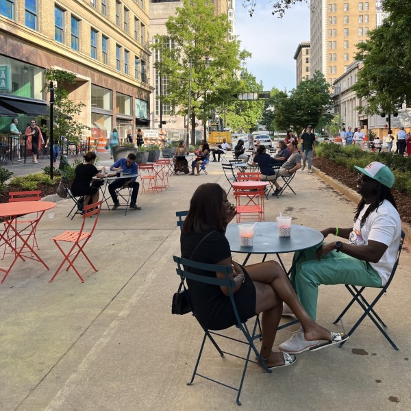 People sitting at café tables set-up along a street lined with tall office buildings.