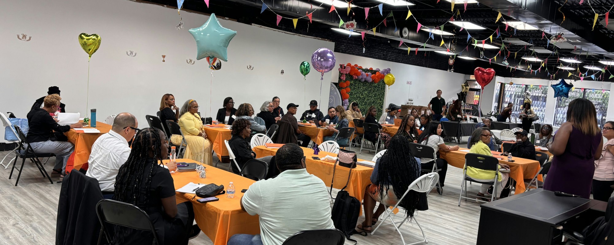Tables of people at an event in a room decorated with pennants and balloons