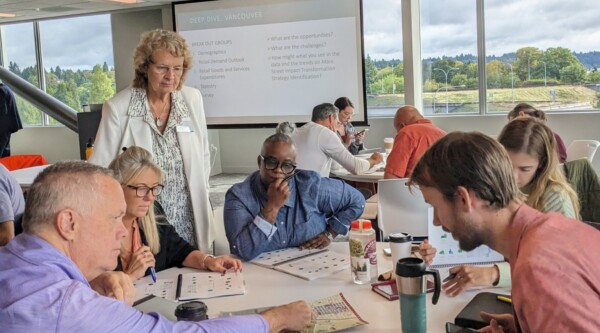People engaged in active discourse while gathered around a table and reviewing materials.