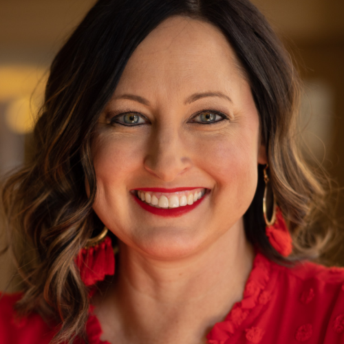 Brunette woman wearing red shirt and red earrings smiles at camera