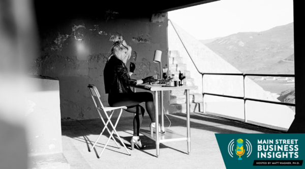 Black and white photo of woman sitting at small work table. In the foreground is a graphic that reads "Main Street Business Insights"