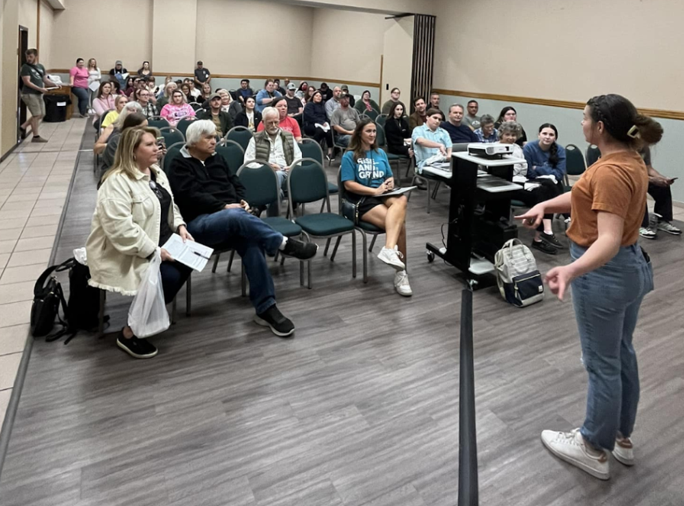 A community engagement meeting with one speaker in front and many people in chairs listening