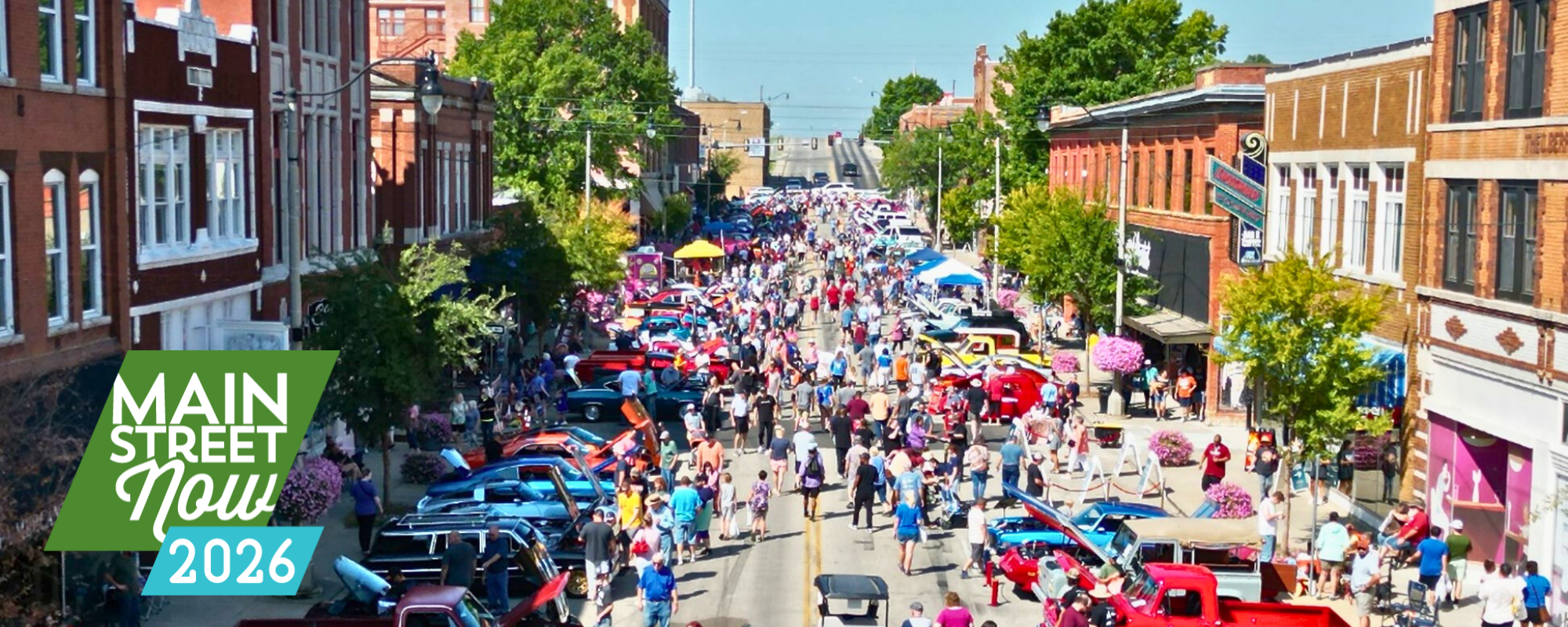 A busy street fair with vintage cars in a historic downtown on a sunny day